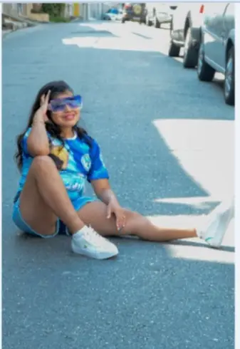 Clara sentada na rua, de óculos azuis