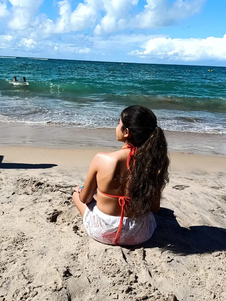 Clara sentada na areia olhando o mar